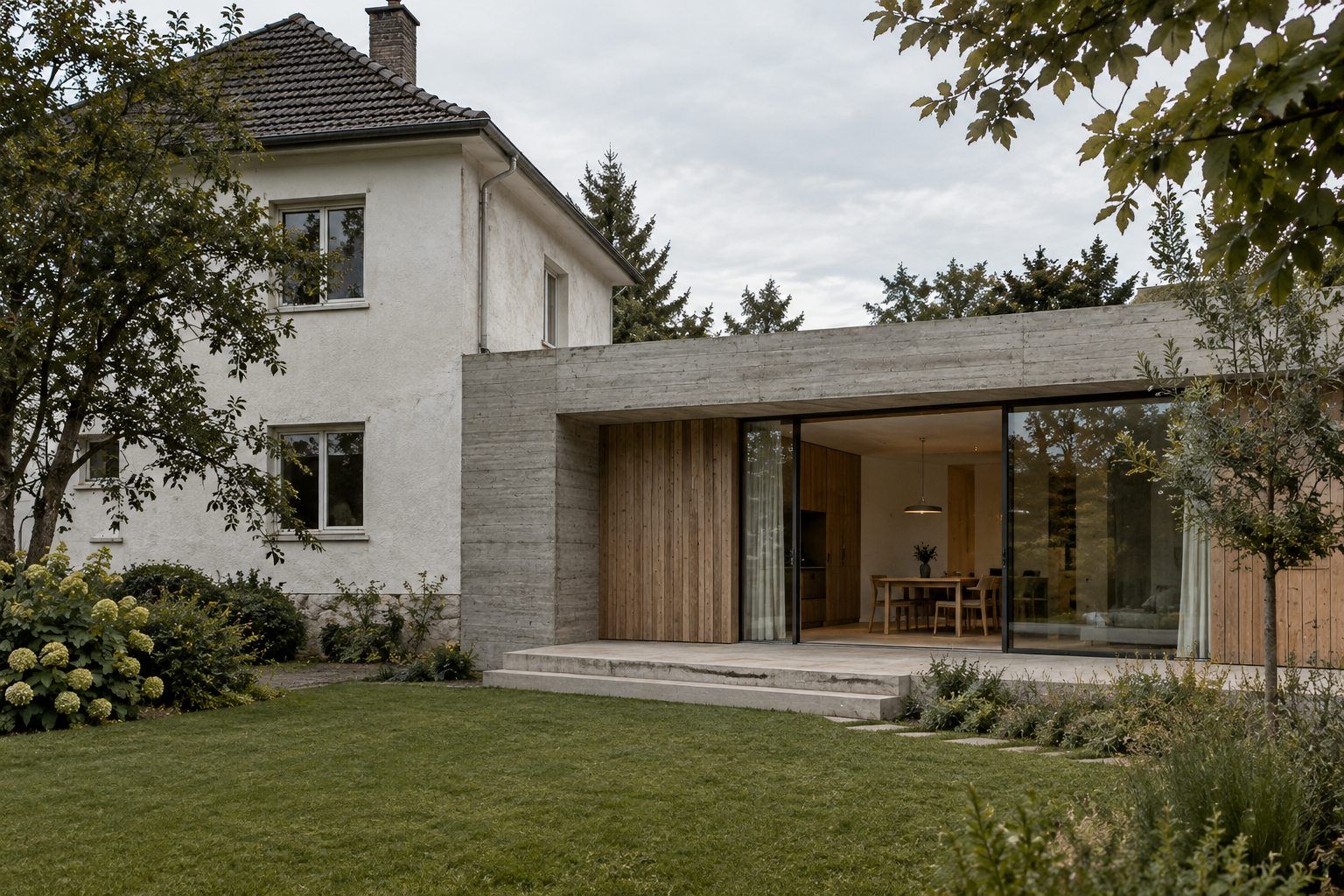 Weiß verputztes Siedlungshaus mit flachem Anbau aus Sichtbeton und Eiche zum Garten